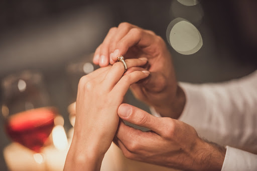 Cropped image of man putting on an engagement ring on his girlfriend's finger while they sitting at the tablet in a restaurant